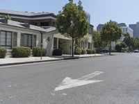 an arrow is pointing to an empty street next to buildings with green trees lining both sides