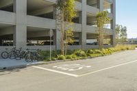 several bicycles parked beside two parked cars next to a parking garages garage at an empty street