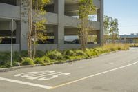 several bicycles parked beside two parked cars next to a parking garages garage at an empty street