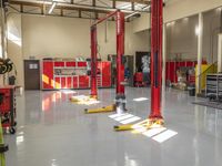 the two scissor lifts are red and yellow in a building with lots of other tools