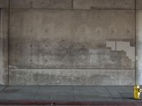 a red fire hydrant sits against a concrete wall and concrete ground in the city