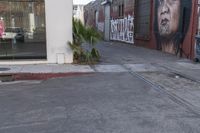 a picture of a man painting on a building near the street and train tracks beside it