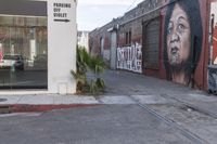 a picture of a man painting on a building near the street and train tracks beside it