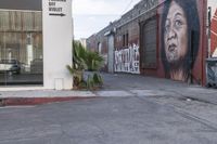 a picture of a man painting on a building near the street and train tracks beside it