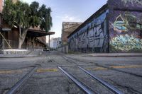 an empty train track in front of graffiti on the side of a building near tracks