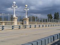 a pedestrian walkway under a dark cloud covered sky and street lights are on the other side of the bridge