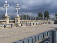 a pedestrian walkway under a dark cloud covered sky and street lights are on the other side of the bridge