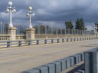 a pedestrian walkway under a dark cloud covered sky and street lights are on the other side of the bridge