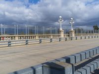 a pedestrian walkway under a dark cloud covered sky and street lights are on the other side of the bridge