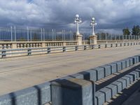 a pedestrian walkway under a dark cloud covered sky and street lights are on the other side of the bridge