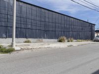 a car is driving down the street near an industrial building in california city with a privacy fence