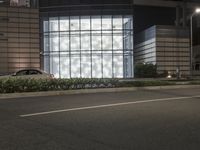 a building has a glass front in a city street, with greenery in front