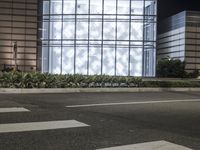 a building has a glass front in a city street, with greenery in front