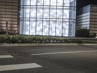 a building has a glass front in a city street, with greenery in front