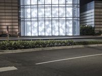 a building has a glass front in a city street, with greenery in front