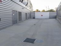 a parking lot with a metal drainage hole on the ground and a white fence and building