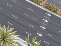 an aerial view looking down at the street where two cars are parked and some are white arrows on a black asphalt road