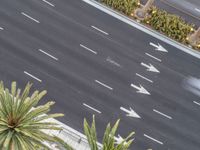 an aerial view looking down at the street where two cars are parked and some are white arrows on a black asphalt road