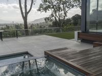 a pool and deck in front of a huge glass wall, with a view over trees to mountains