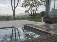 a pool and deck in front of a huge glass wall, with a view over trees to mountains