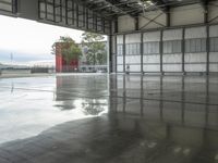 a wet floor in an empty building with red and white walls behind it and several trees