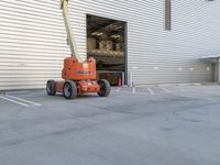 a fork lift parked outside a building on cement flooring area with a large white door and two garages in the background