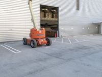 a fork lift parked outside a building on cement flooring area with a large white door and two garages in the background