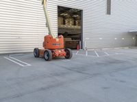 a fork lift parked outside a building on cement flooring area with a large white door and two garages in the background