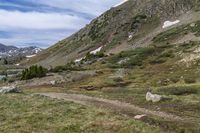 two people with backpacks walking on a trail in the mountains near a lake and mountain range