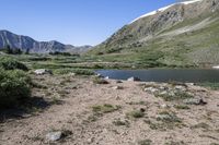 a large lake surrounded by rocky mountains with pine trees in the foreground and sparse vegetation around