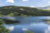 a mountain sits in the background on a sunny day above the water and on top of a hill is a blue lake and green trees