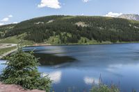 a mountain sits in the background on a sunny day above the water and on top of a hill is a blue lake and green trees