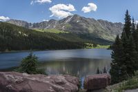 a body of water surrounded by mountains on a sunny day to the side, surrounded by large rocks with trees