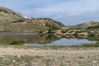 a woman is standing next to her bicycle near a lake with snow capped hills behind