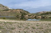 a woman is standing next to her bicycle near a lake with snow capped hills behind