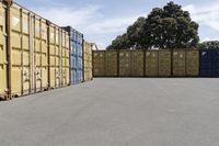 a group of multiple containers with trees behind them in a parking lot next to the road