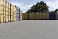 a group of multiple containers with trees behind them in a parking lot next to the road