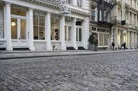 a paved cobblestone street and brick buildings in the city with people walking on the sidewalk