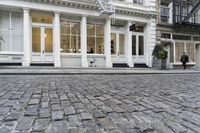 a paved cobblestone street and brick buildings in the city with people walking on the sidewalk