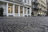 a paved cobblestone street and brick buildings in the city with people walking on the sidewalk