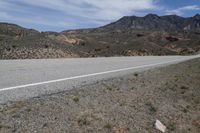 a dirt road with rocky terrain and mountains in the distance, with bushes on either side of the road