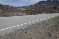 a dirt road with rocky terrain and mountains in the distance, with bushes on either side of the road