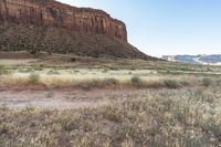 man riding a horse in the wilderness near tall hills, grass, and cliffs above it