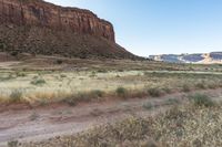 man riding a horse in the wilderness near tall hills, grass, and cliffs above it