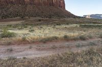 man riding a horse in the wilderness near tall hills, grass, and cliffs above it