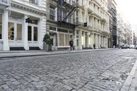 a paved cobblestone street and brick buildings in the city with people walking on the sidewalk