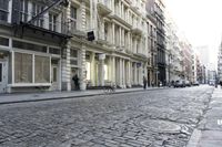 a paved cobblestone street and brick buildings in the city with people walking on the sidewalk