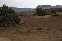 a black motorcycle parked in dirt near mountains and trees on a cloudy day, with a sign pointing to the right