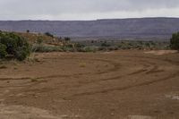 a black motorcycle parked in dirt near mountains and trees on a cloudy day, with a sign pointing to the right