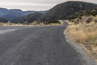 an empty mountain road with rocks and grass near it and two motorcycles parked in front of the road